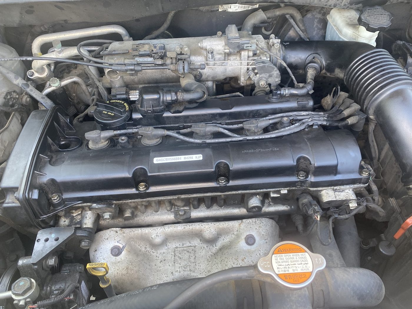 A four cylinder engine bay photographed from above with the hood up, plug leads and valve cover in view