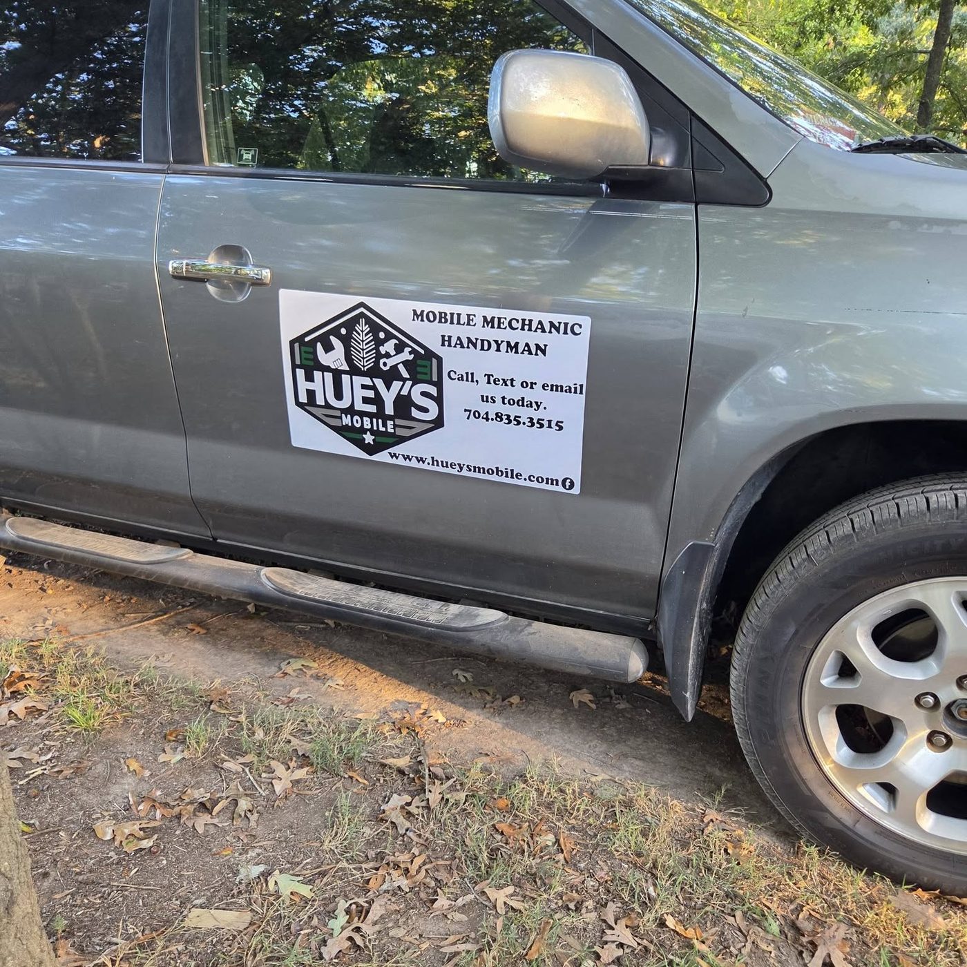 The Huey's Mobile magnetic sign on the door of his gray SUV, parked under trees on a dirt shoulder